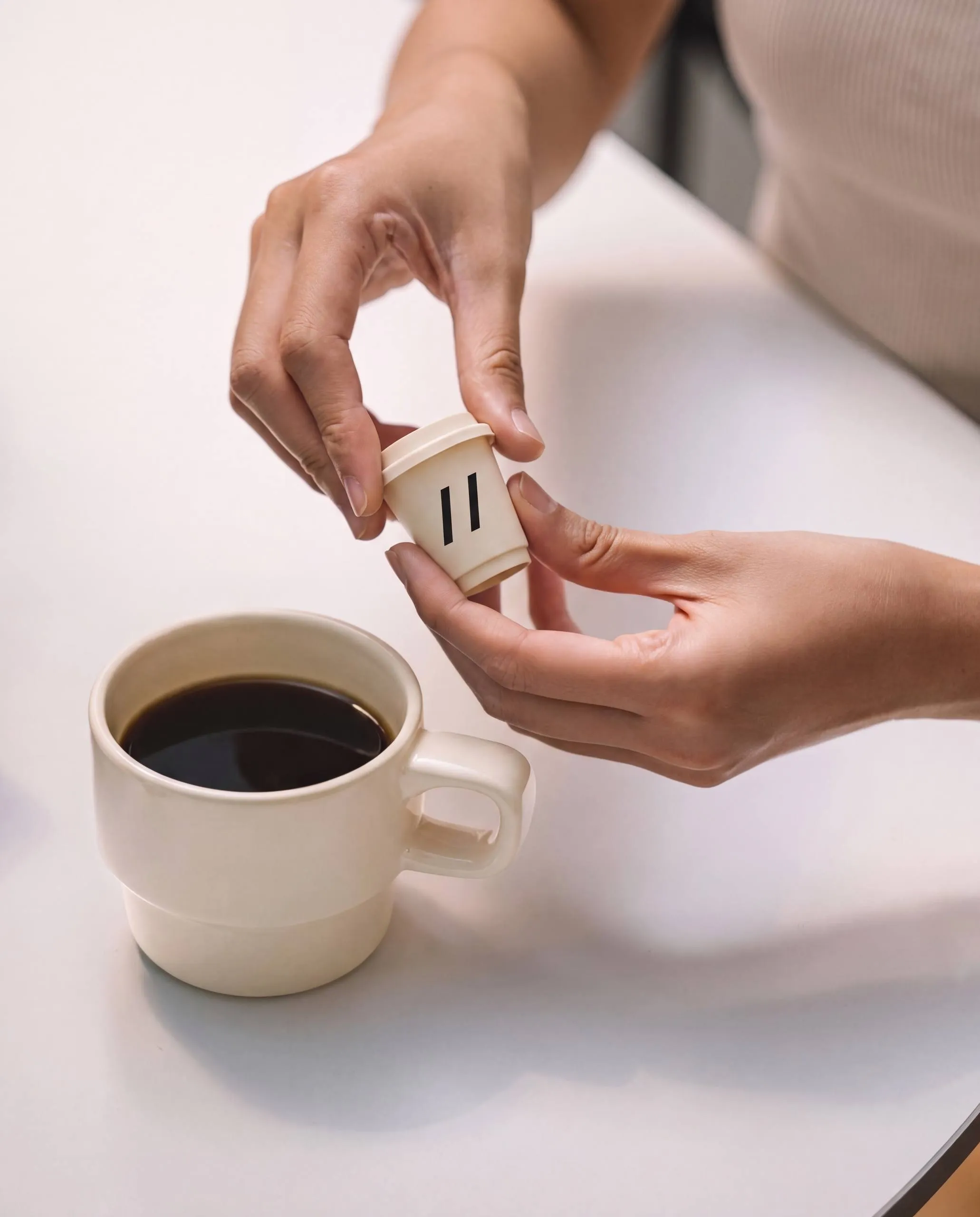 Hands opening a Parallel instant coffee cup beside a mug of black coffee